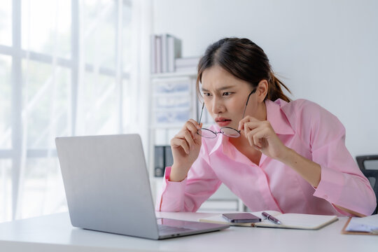 Portrait of upset Asian businesswoman at desk in office.  Asian stressed businesswoman feeling strain in eyes after working for long hours on computer.