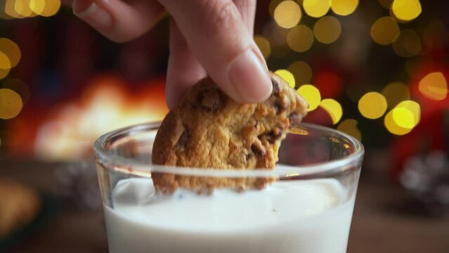 Dunking a Chocolate Chip Cookie in Glass of Milk in Slow Motion, Christmas Atmosphere by the Fireplace
