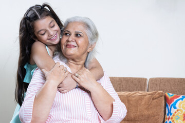 Cute caring small Indian granddaughter embrace cuddle smiling middle-aged 60s grandmother, little grandchild hug senior grandparent, show love and gratitude, family unity concept