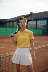 Young woman tennis player in trendy fashion sportswear posing with racket