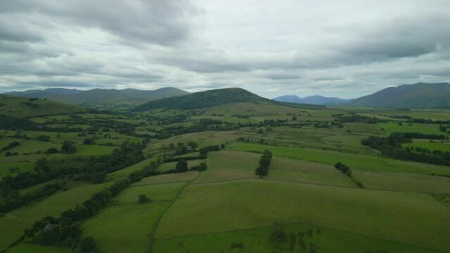 Flying high over green English countryside on cloudy summer day towards the hill Great Mell Fell, English Lake District, Cumbria, UK.