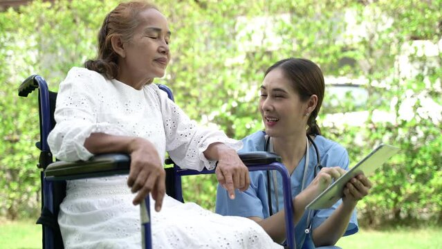 Senior lady patient sitting on wheelchair talking to caring female nurse at home. Concept of wellness consultation, caregiver, elderly healthcare and homeopathic doctor.
