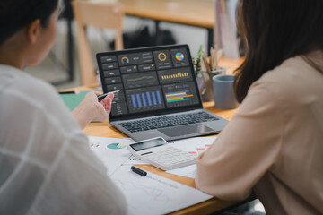 Two businesspeople or an accountant team are analyzing data charts, graphs, and a dashboard on a laptop screen in order to prepare a statistical report and discuss financial data in an office. - obrazy, fototapety, plakaty