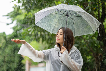 Happy Asian beautiful woman holding umbrella in raining season while standing in the park. She...