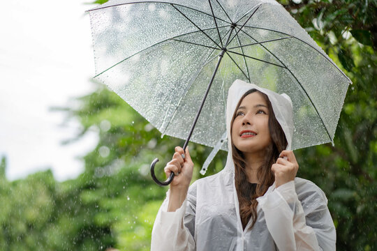 Happy Asian beautiful woman holding umbrella in raining season while standing in the park. Lifesyle Concept.