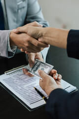 Fototapeta premium Businessmen shaking hands and accepting bribes under the table concept of corruption