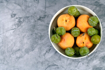 White bowl with summer fruit peaches and green plums