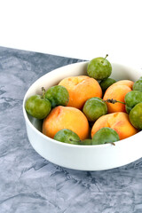 White bowl with summer fruit peaches and green plums