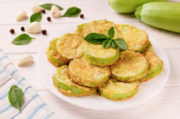 Baked zucchini with cheese, garlic and fresh herbs on a white wooden background.