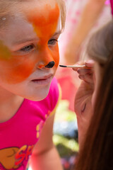 The face of a girl painted with colorful paints. Painting children's faces during a family picnic.