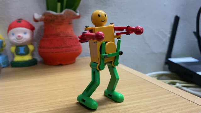 Retro wind up toy robot smiling face dancing by clockwork motor on wooden table