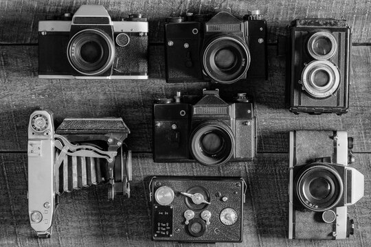Set of vintage film camera from the times of the USSR on a wooden background, closeup, top view. Line of old retro cameras. Black and white