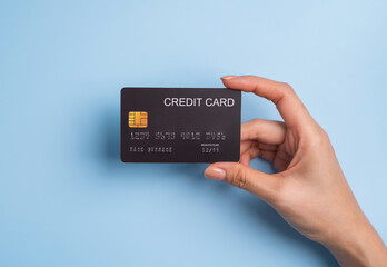 Top view of hand holding black credit card on blue background.