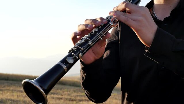 Clarinetists teenager plays the clarinet in the mountains at sunset. Middle Eastern type guy deja musical wind instrument will press the keys and make a beautiful sound outdoors