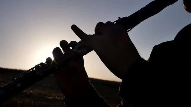 Close-up silhouette of the fingers of a musician playing the clarinet in the evening at sunset in the mountains. The fingers of a young clarinetist press the keys in the background the sun glares 