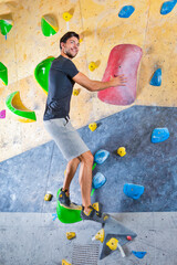 Obraz na płótnie Canvas Professional Male Rock climber man hanging on a bouldering climbing wall, inside on colored hooks.