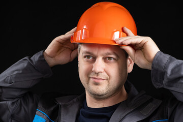 A young man construction worker in a safety helmet and work uniform on a black background