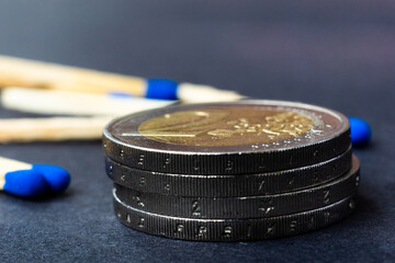 Blue matches and stack of coins on dark background macro