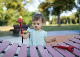 Little girl playing big xylophone at city park. Toddler playing outside.