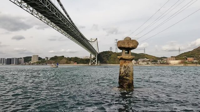 Beautiful Old japanese rock lantern halfly submerged in water in  front of  Kanmon bridge and the kanmon strait in between the japanese island Honshu and Kyushu