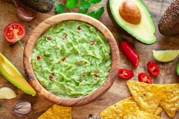 Guacamole, guacamole ingredients and chips on wooden background.  Flat lay.