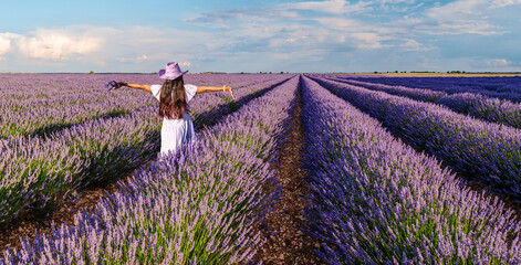 Young girl walking  in the lavender field and stunning sunset sky at the background. Brihuega,...
