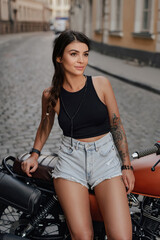 Stunning brunette sitting on her retro motorcycle against in the middle of a street in Europe