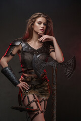 Stunning Viking girl dressed in a chainmail top and fur skirt poses with a two-handed axe against a textured gray wall