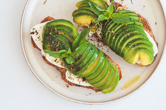 Breakfast toast with cream cheese and avocado on white plate, white background. Healthy food concept.