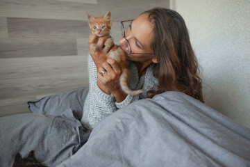Beautiful woman dressed warm swetr and pijamas trousers playong with cat in the bed