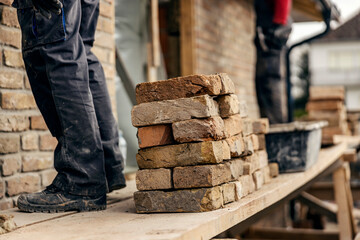 Pile of bricks on a scaffolding with workers building a brick wall.