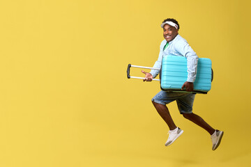 Fototapeta na wymiar An African-American man in a stylish cap, sneakers and shirt rushes towards adventures on a yellow background with a blue suitcase. A happy guy with blue suitcases is going on an exciting travel