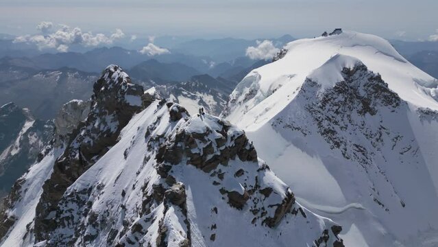 two alpinists mountaineers standing on a mountain summit, during morning sunrise, with dramatic mountains in the backgroud. Dufourspitze, Monte Rosa, Switzerland. Aerial drone Point of interest