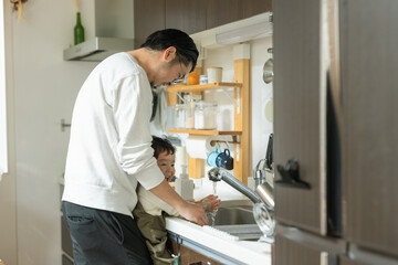 春の天気の良い日中の台所で笑顔で手を洗う子どもと手伝う父親