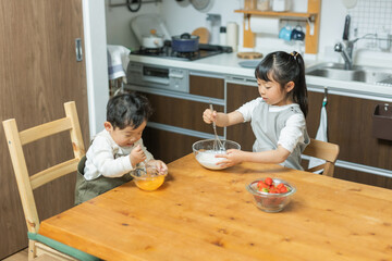 秋の日中の台所で料理の手伝いで泡立て器でクリームと卵を混ぜるアジア人の子ども達