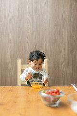 春のキッチンでテーブルに座って楽しそうに泡立て器で卵を混ぜる日本人の男の子