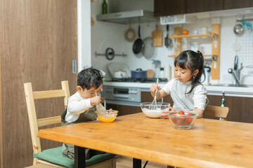 春の昼間のキッチンで二人で仲良くお菓子作りの手伝いをする日本人の幼い兄弟 - obrazy, fototapety, plakaty