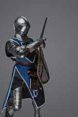 Medieval knight in active battle pose, wielding sword and shield against gray background