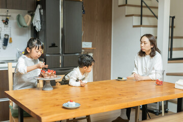 秋の日中、キッチンで座ってケーキを食べるアジア人の兄弟と見守る母親