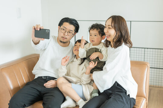 春の明るい日中、ソファに座ってスマートフォンで家族写真を自撮りする日本人の家族