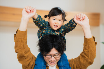 春の昼間に手を繋いで父親に肩車されて正面を向く日本人の小さな子ども