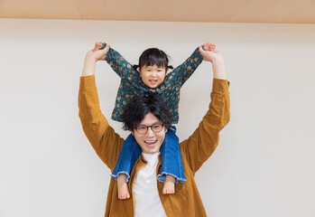 Fototapeta na wymiar 春の日中、家の中で肩車して正面を向いて笑う日本人のパパと娘の親子