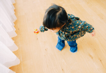 秋の日中、カーテンの近くでおもちゃを握って立つ日本人の幼い女の子