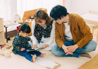 冬の日中、おもちゃが溢れるリビングの床に座りながら絵本の読み聞かせをする日本人親子の家族写真
