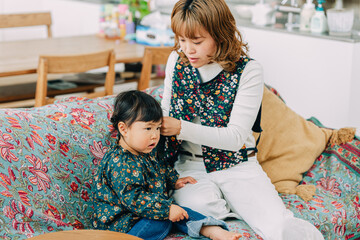 春の昼間、リビングのソファで娘の髪の毛を結う日本人の30代女性