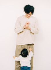 秋の日中、白い壁の前で足元でしがみつく幼い娘を見つめる日本人の男性