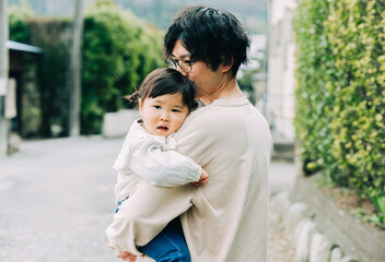 春の朝、屋外で小さい赤ちゃんを抱っこする眼鏡をかけた日本人の30代のお父さん - obrazy, fototapety, plakaty
