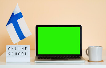 Open laptop with green screen chroma key on the table next to the flag of Finland and a display...