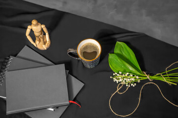 dark wooden dark notebooks, a cup of coffee, a bouquet of lilies of the valley and a sitting...