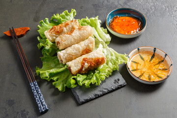 Nems sur une ardoise avec des baguettes et diverses sauces. Cuisine vietnamienne. 